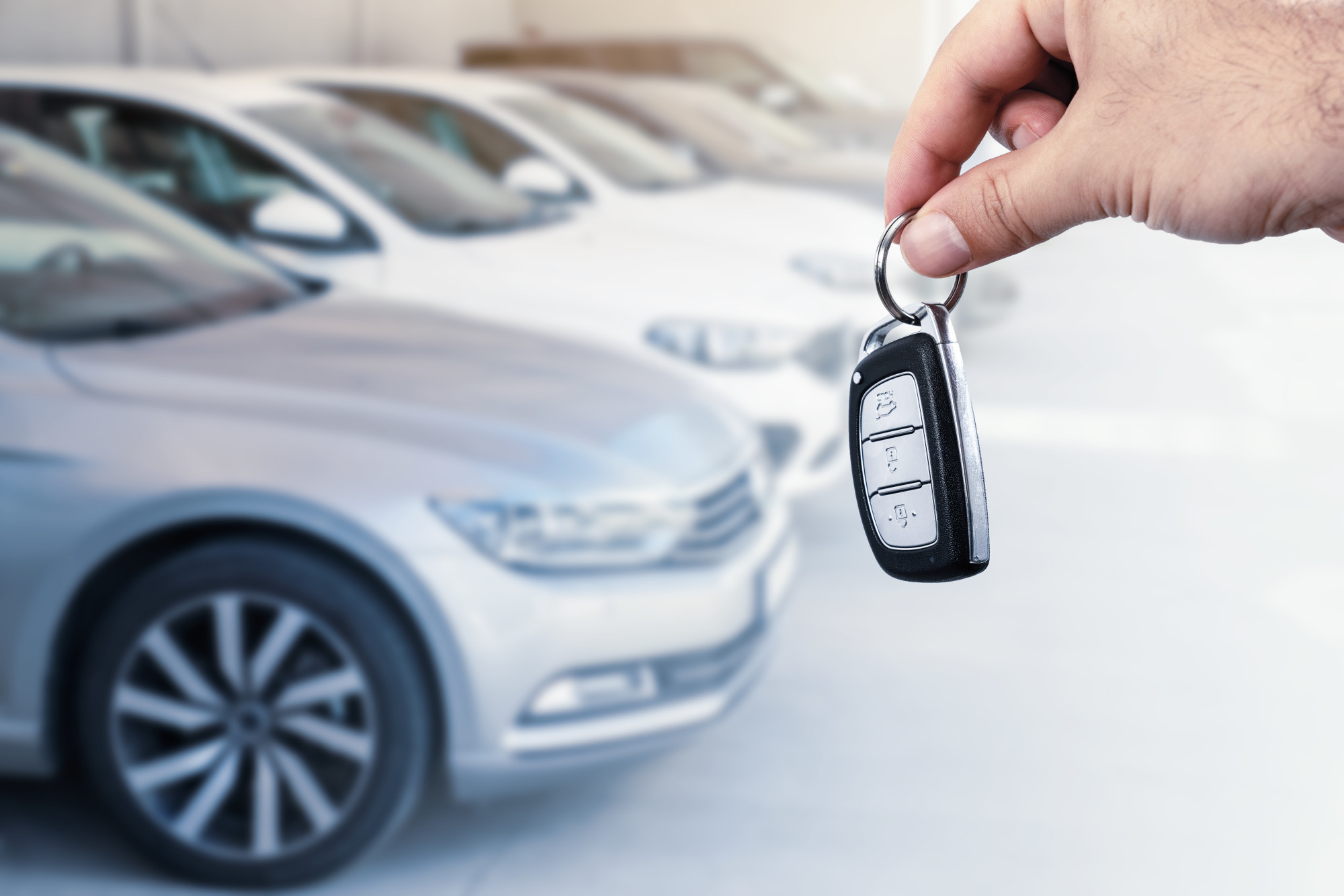 person holding car keys with row of autos